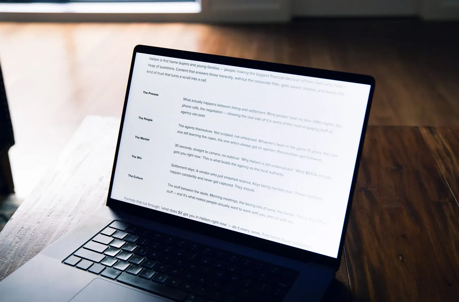 A brief document open on a laptop screen, on a timber desk