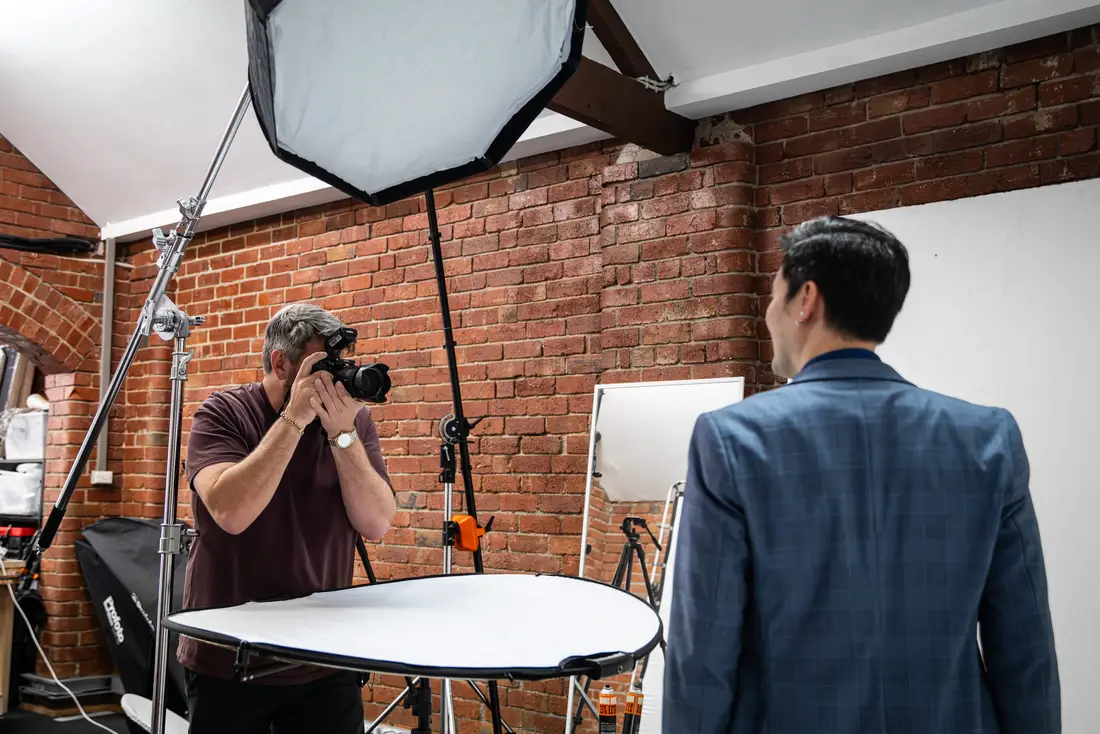 A photographer shooting a portrait in the brick-wall studio with a softbox and reflector