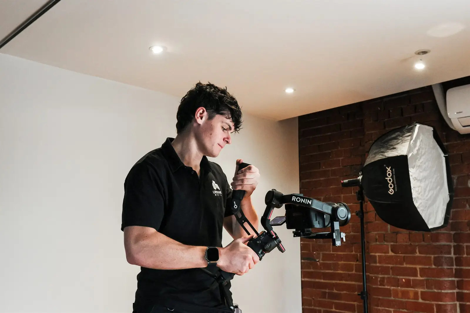 A camera operator in black holding a gimbal camera rig in a studio with a softbox