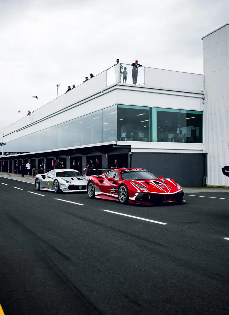 A red Ferrari leaving the pit lane beside a white car